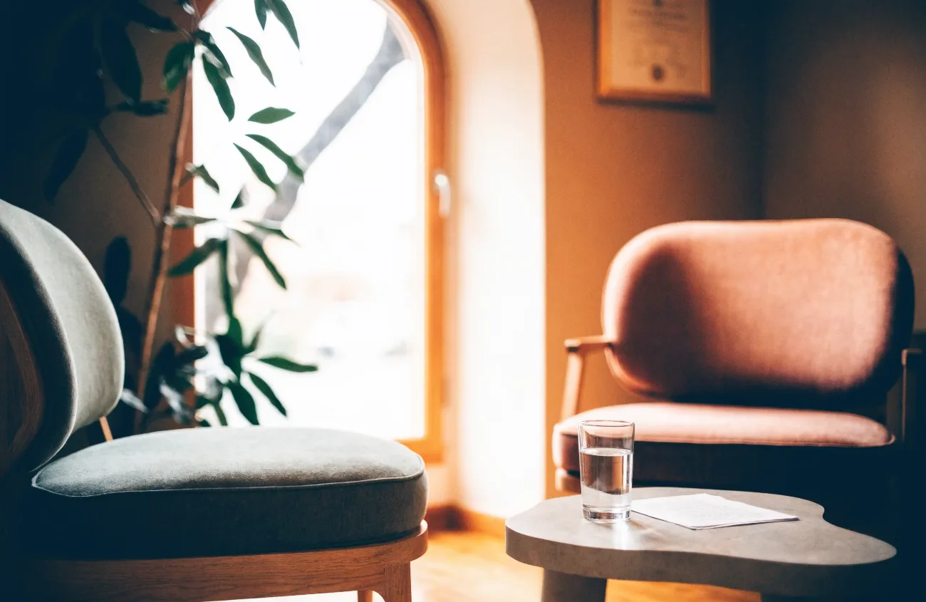 Consulting room two at Alder House: two chairs facing each other, a glass of water on a low table, daylight through an arched window.
