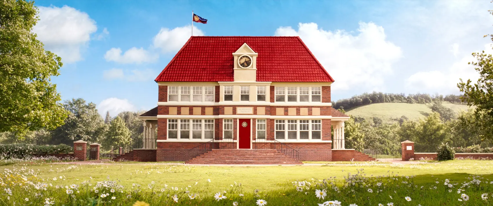 Meadow Lane Primary School: a red-brick building with a cherry-red roof and a little clock tower with a flag, set in a wildflower meadow with trees and rolling Surrey hills under a bright blue sky.
